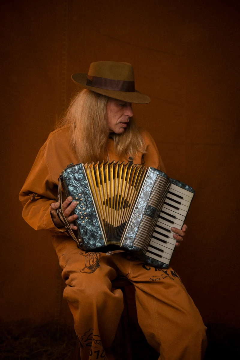 Sanfoneiro de chapéu e macacão da coleção Brasil Rural, tocando sentado no barracão