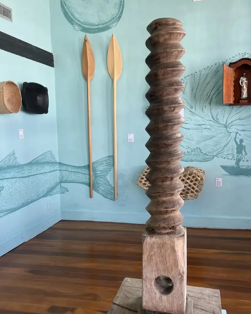 Sala da exposição do Glossário Caiçara de Paraty, com monjolo de rosca e pinturas de peixes na parede